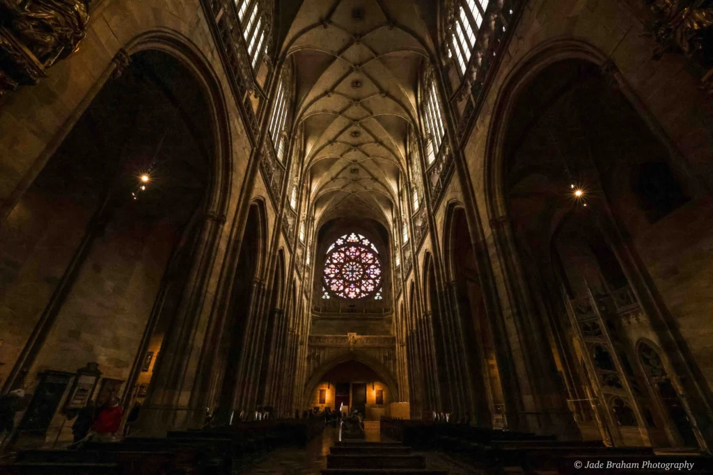 Prague Cathedral has a long aisle with a stained glass window at the end.