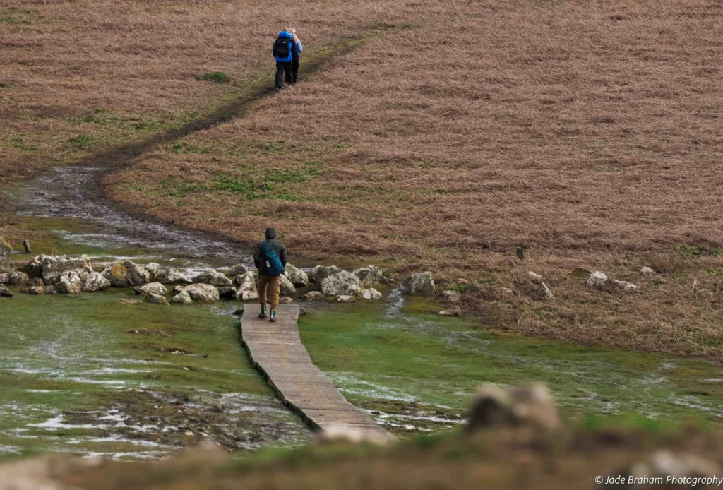 A man is walking over a wooden walkway in the Wick Stream