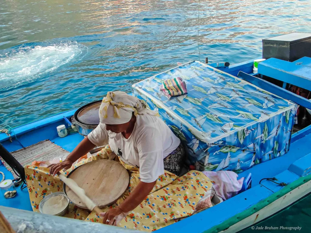 A woman is making pancakes in a boat. 