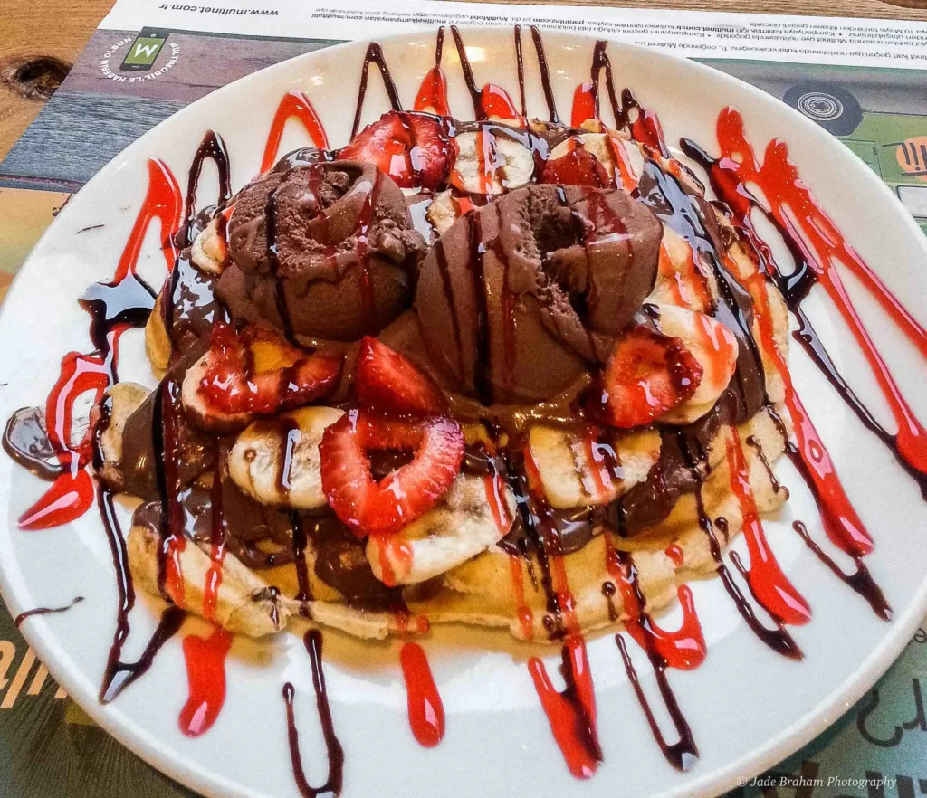 There is a pancake covered with chocolate sauce, bananas, strawberries and chocolate ice cream. 