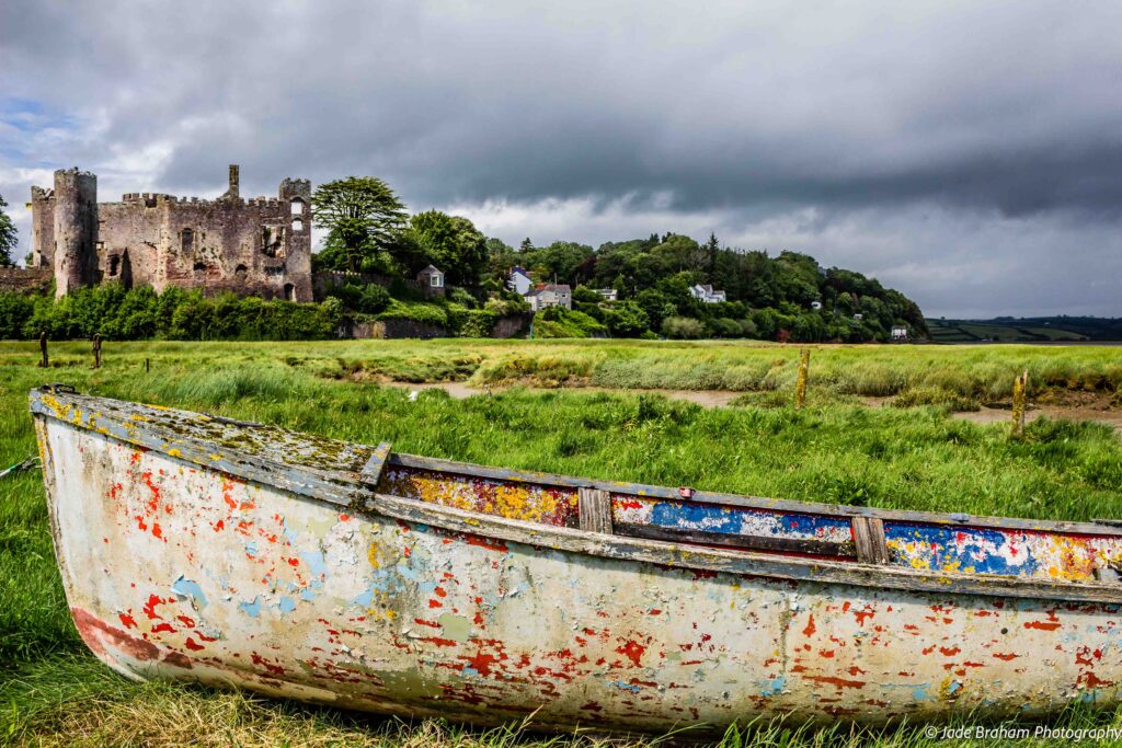 Laugharne Castle can be see from the river with an old fishing boat in front of it. 