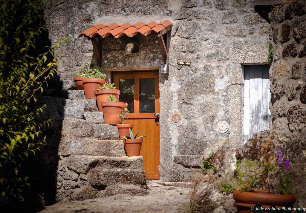 A charming entrance to a home with steps, potted plants and a terracotta roof. 