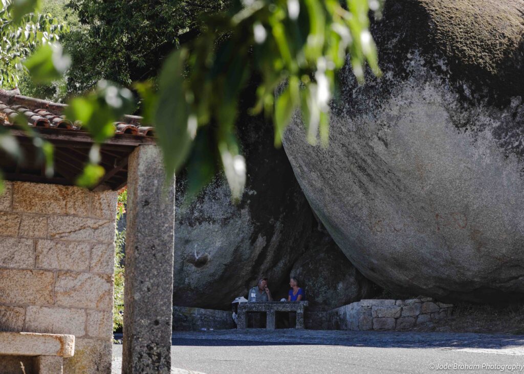 A couple sits at a picnic table underneath two enormous boulders.